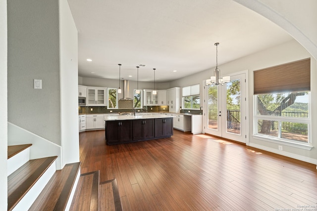 kitchen with stainless steel microwave, wall chimney range hood, dark wood-type flooring, pendant lighting, and a center island