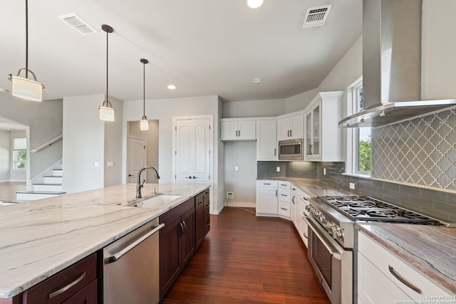 kitchen with dark hardwood / wood-style floors, appliances with stainless steel finishes, wall chimney range hood, decorative light fixtures, and sink