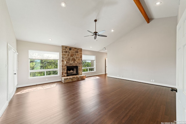 unfurnished living room featuring ceiling fan, wood-type flooring, beamed ceiling, and a stone fireplace