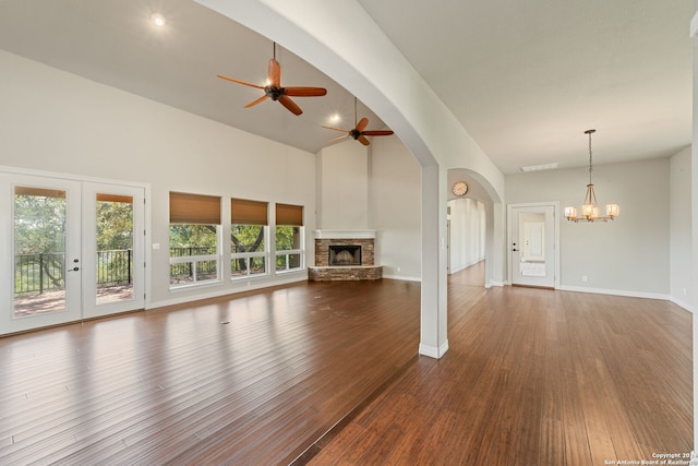 unfurnished living room with high vaulted ceiling, ceiling fan with notable chandelier, french doors, a stone fireplace, and hardwood / wood-style flooring