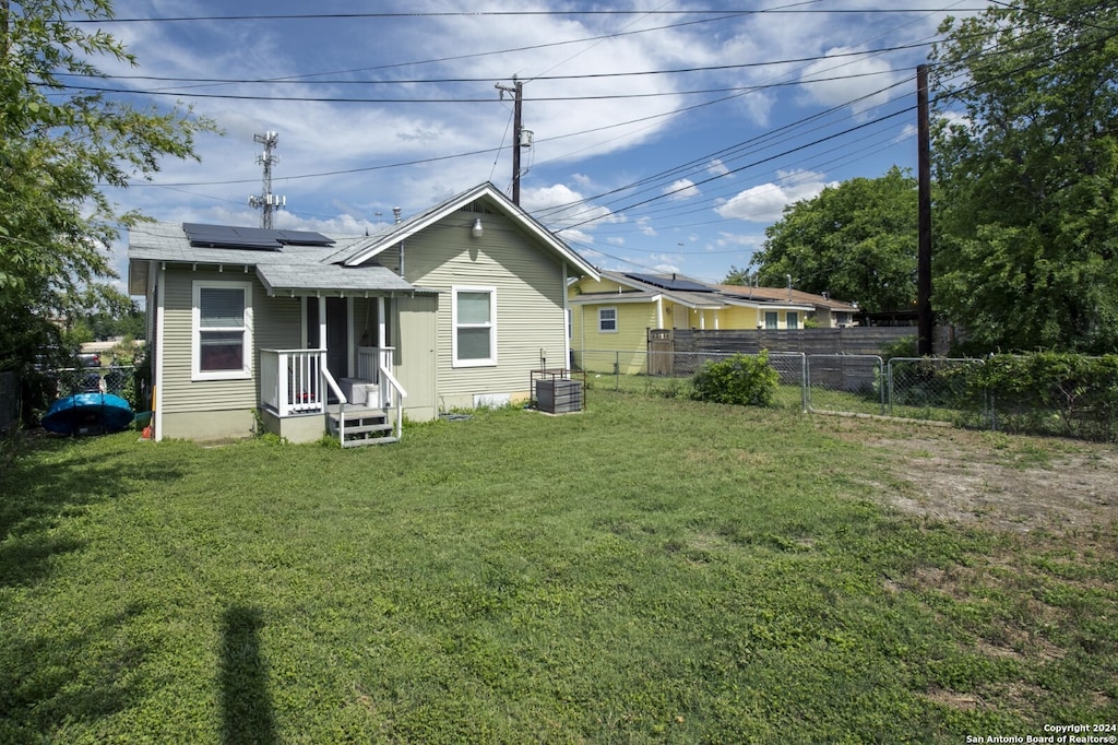 rear view of house with central AC unit, solar panels, and a yard