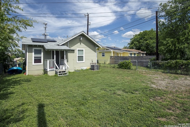 rear view of house with central AC unit, solar panels, and a yard