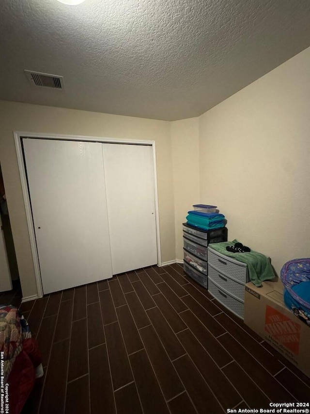 unfurnished bedroom featuring dark wood-type flooring, a textured ceiling, and a closet