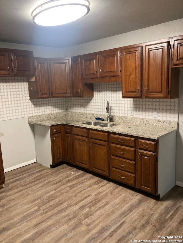 kitchen with backsplash, light stone countertops, wood finished floors, and a sink