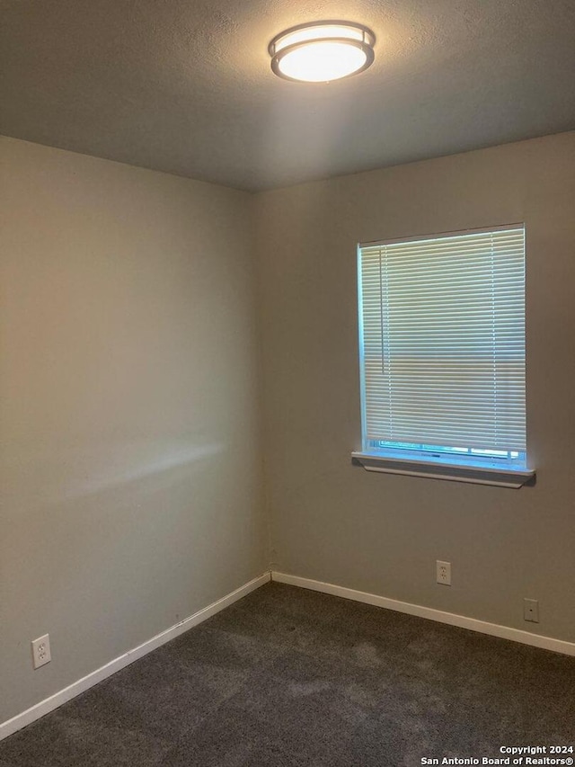 spare room featuring baseboards, dark colored carpet, and a textured ceiling