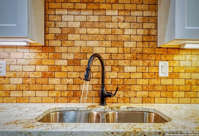 interior details featuring white cabinets, sink, and light stone counters