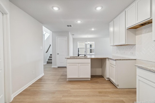 kitchen featuring sink, kitchen peninsula, light hardwood / wood-style floors, decorative backsplash, and white cabinets