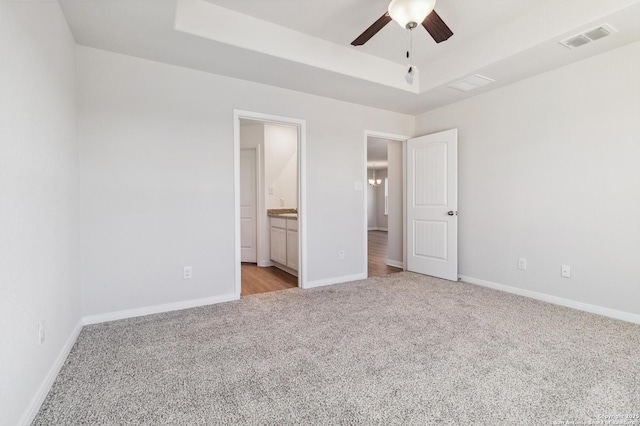 unfurnished bedroom with a raised ceiling, connected bathroom, ceiling fan, and light carpet