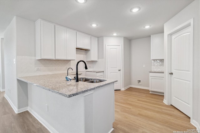 kitchen featuring kitchen peninsula, light wood-type flooring, white cabinetry, and sink