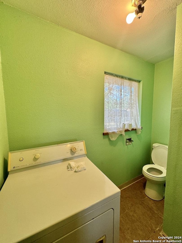 washroom with washer / clothes dryer, dark tile patterned floors, and a textured ceiling