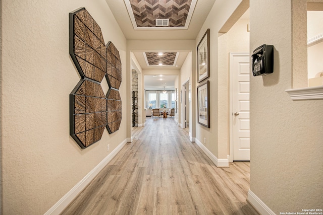 corridor featuring a tray ceiling and light wood-type flooring