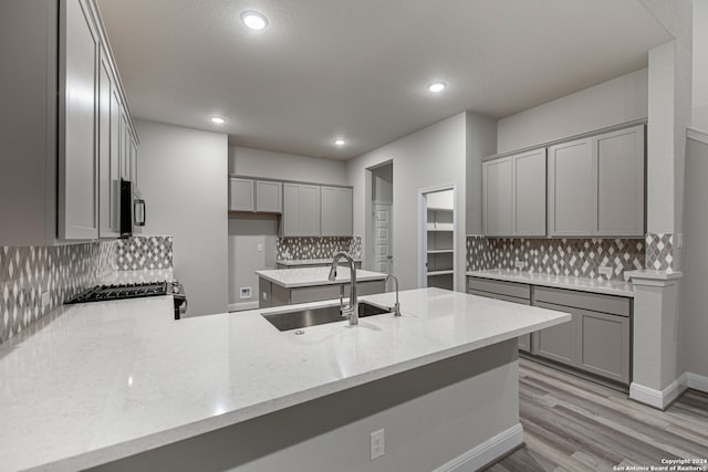 kitchen featuring backsplash, light hardwood / wood-style flooring, light stone counters, and sink