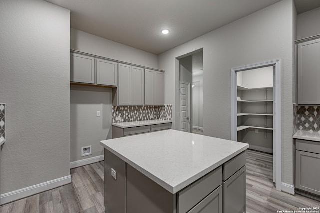 kitchen featuring gray cabinetry, light wood-type flooring, a kitchen island, and backsplash