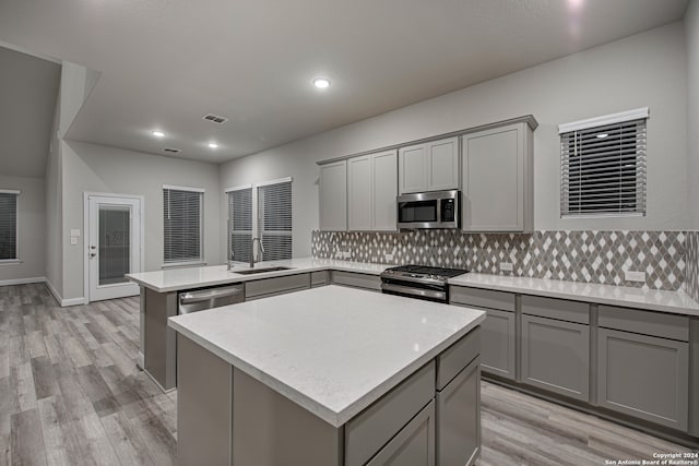 kitchen featuring decorative backsplash, appliances with stainless steel finishes, a center island, and gray cabinets