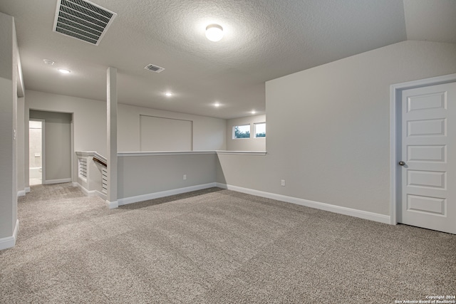 spare room with a textured ceiling, lofted ceiling, and light colored carpet