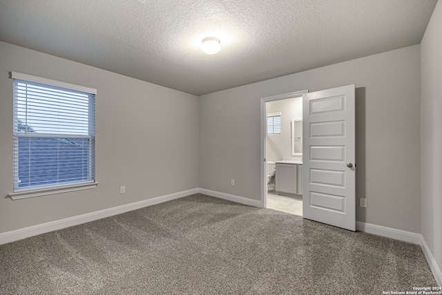 unfurnished bedroom featuring light carpet, a textured ceiling, and connected bathroom