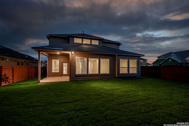 back house at dusk with a yard and a patio area