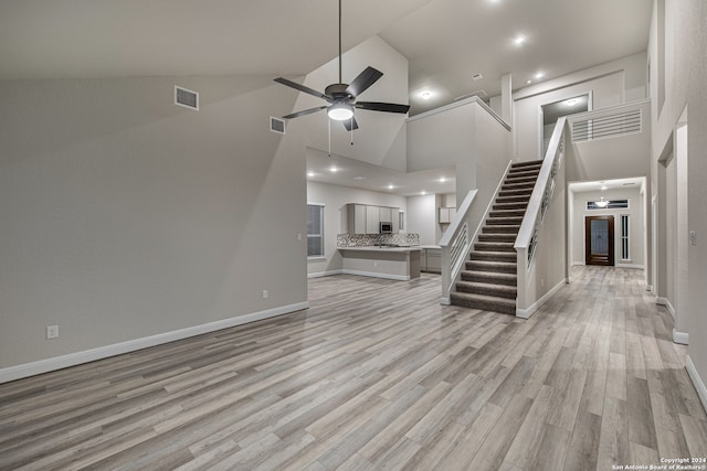 unfurnished living room featuring ceiling fan, high vaulted ceiling, and light wood-type flooring