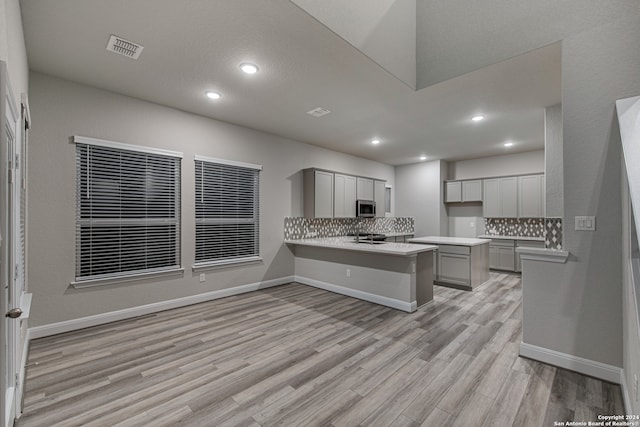 kitchen featuring kitchen peninsula, gray cabinets, tasteful backsplash, and light hardwood / wood-style floors