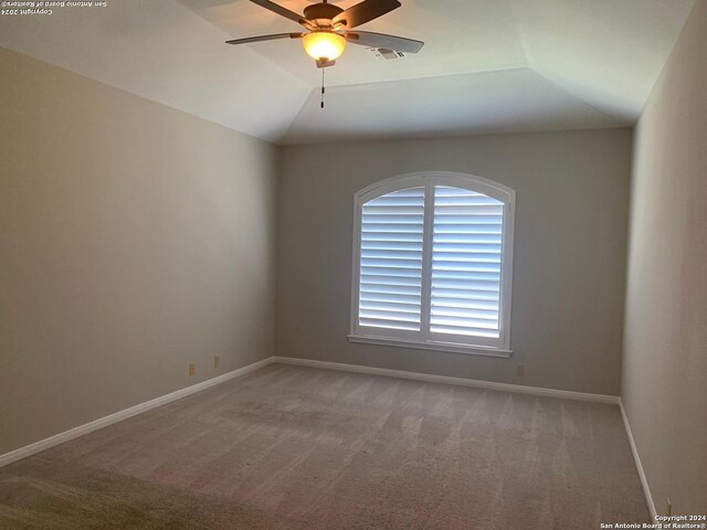 carpeted empty room featuring a ceiling fan, visible vents, vaulted ceiling, and baseboards