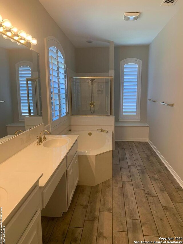 bathroom featuring wood finish floors, visible vents, baseboards, a bath, and a stall shower