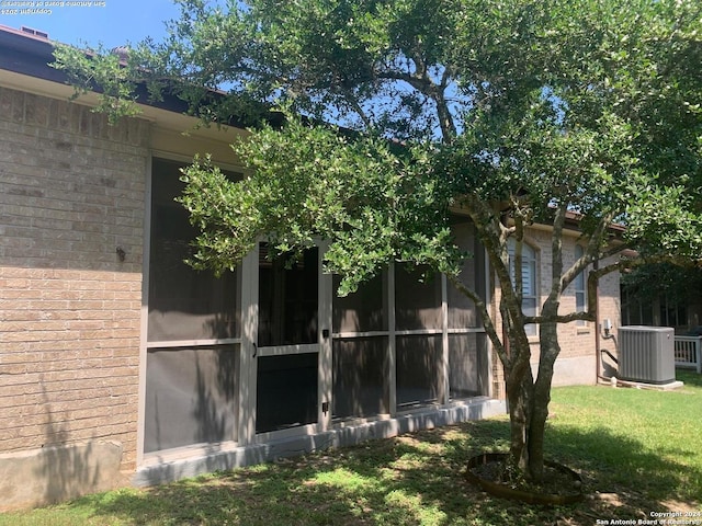 view of side of home featuring brick siding, a yard, and central AC