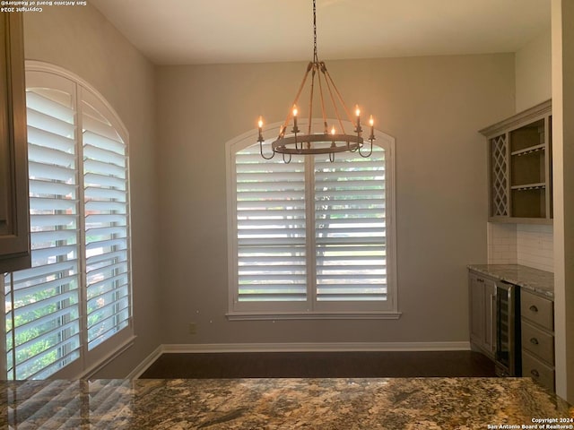 unfurnished dining area featuring plenty of natural light, beverage cooler, baseboards, and a notable chandelier