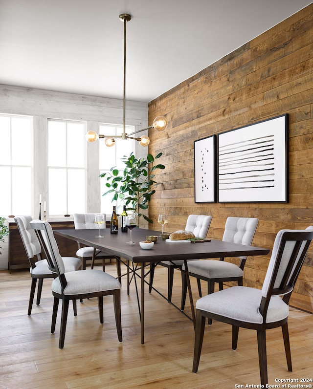 dining room featuring a chandelier, light hardwood / wood-style flooring, and wood walls