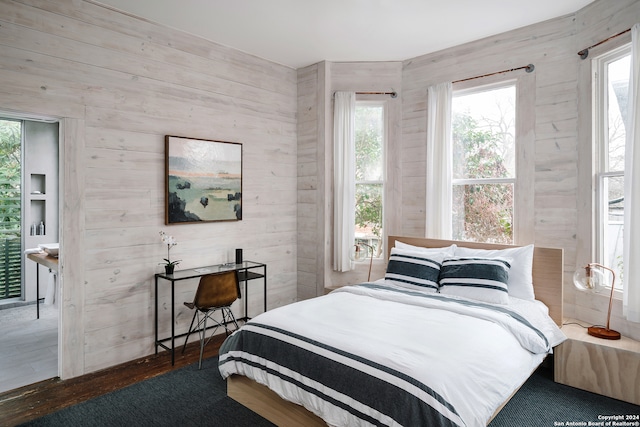 bedroom featuring multiple windows, dark hardwood / wood-style floors, and wooden walls