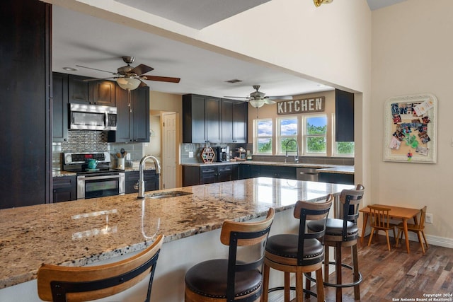 kitchen with sink, stainless steel appliances, light stone counters, tasteful backsplash, and dark hardwood / wood-style flooring