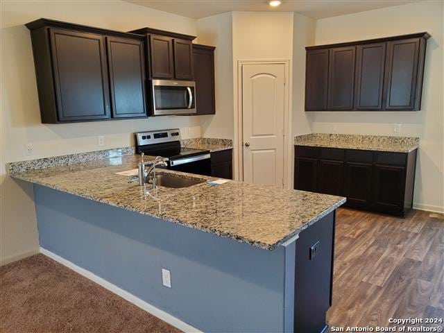 kitchen featuring appliances with stainless steel finishes, light stone countertops, dark carpet, sink, and dark brown cabinetry