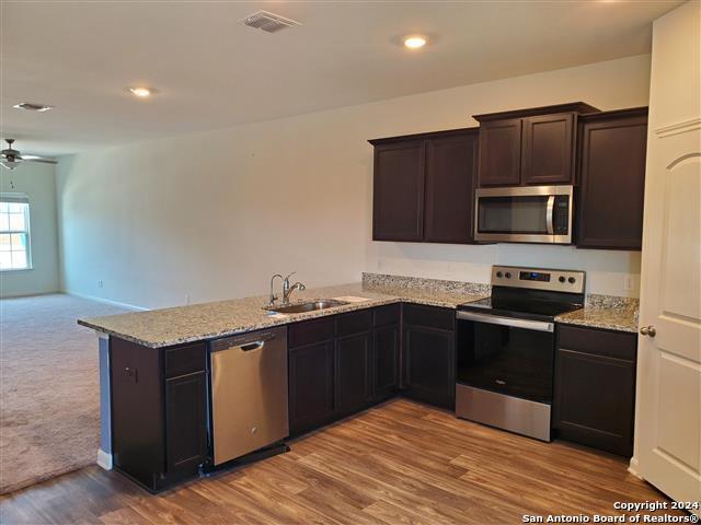 kitchen with sink, ceiling fan, appliances with stainless steel finishes, light stone countertops, and kitchen peninsula