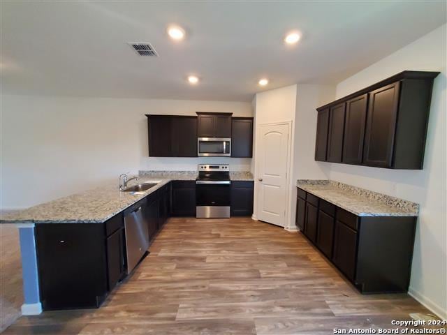 kitchen with light stone counters, appliances with stainless steel finishes, kitchen peninsula, light wood-type flooring, and sink