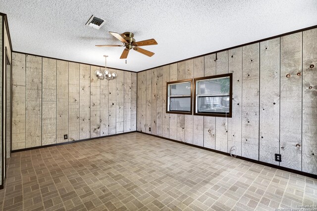 spare room featuring a textured ceiling, wooden walls, and ceiling fan with notable chandelier