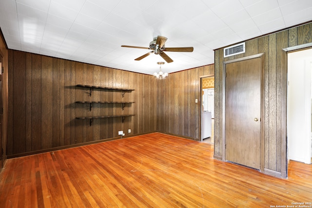 spare room featuring ceiling fan with notable chandelier, wooden walls, and light hardwood / wood-style floors