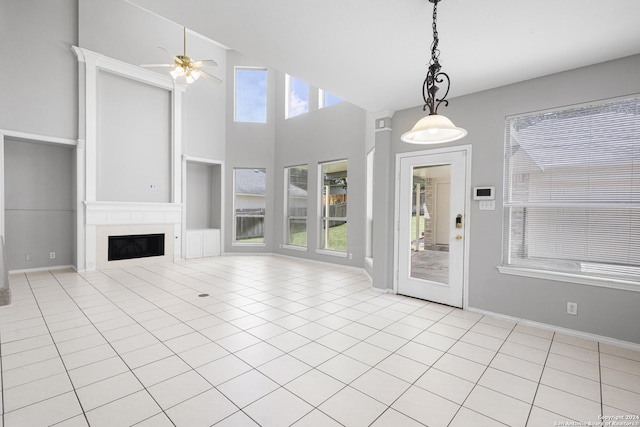 unfurnished living room featuring a towering ceiling, ceiling fan, a fireplace, and light tile patterned floors