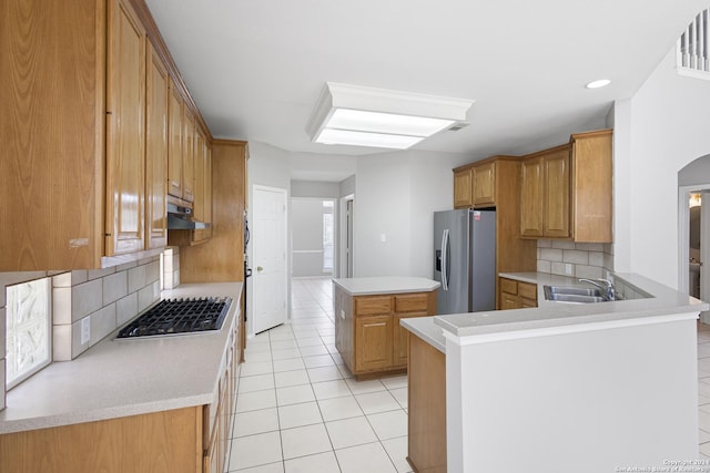 kitchen featuring sink, appliances with stainless steel finishes, a kitchen island, light tile patterned flooring, and kitchen peninsula