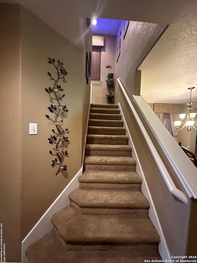 stairway with baseboards, a notable chandelier, and a textured ceiling