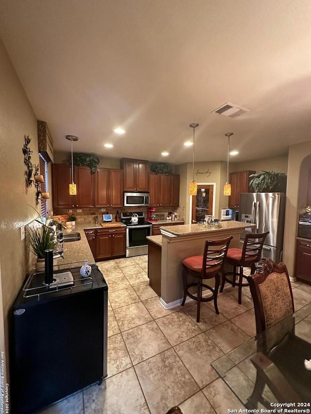 kitchen with pendant lighting, light stone counters, a center island, a kitchen breakfast bar, and stainless steel appliances