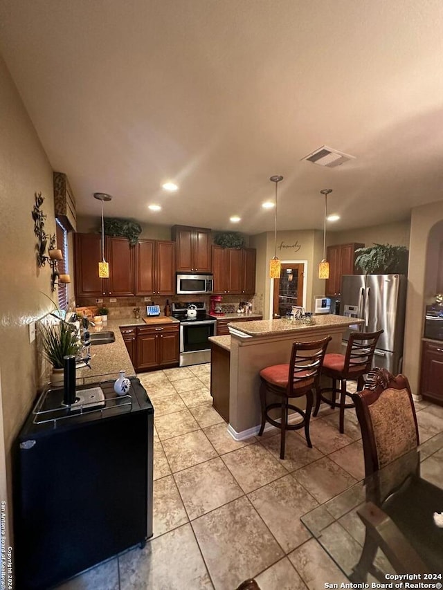 kitchen with a sink, a kitchen bar, appliances with stainless steel finishes, visible vents, and decorative light fixtures