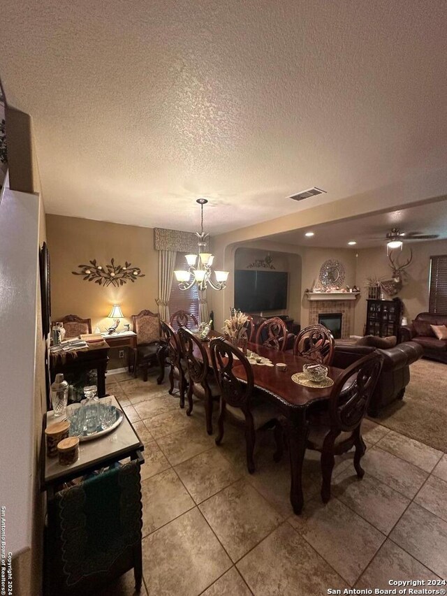 dining area with light tile patterned flooring, a notable chandelier, a tiled fireplace, a textured ceiling, and visible vents