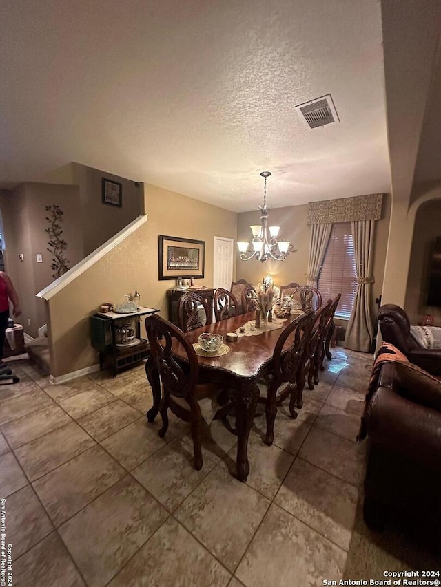tiled dining space with stairs, a textured ceiling, visible vents, and a chandelier