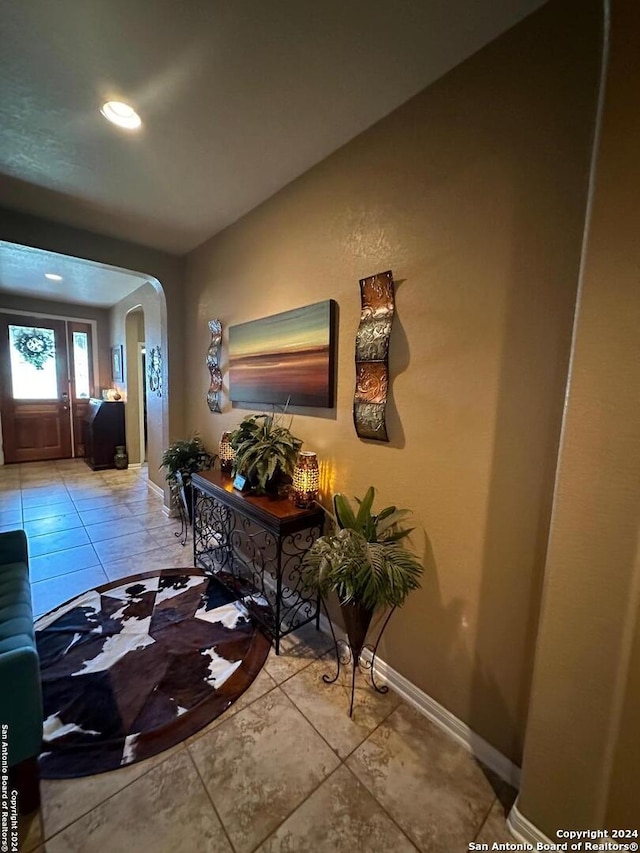 foyer featuring baseboards, arched walkways, and light tile patterned floors