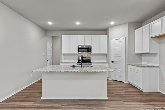 kitchen with light stone counters, stainless steel appliances, white cabinets, and a center island with sink