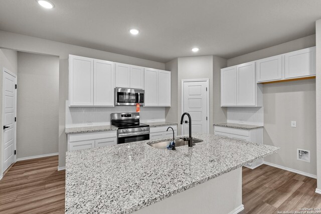 kitchen with tasteful backsplash, stainless steel appliances, hardwood / wood-style flooring, and light stone countertops