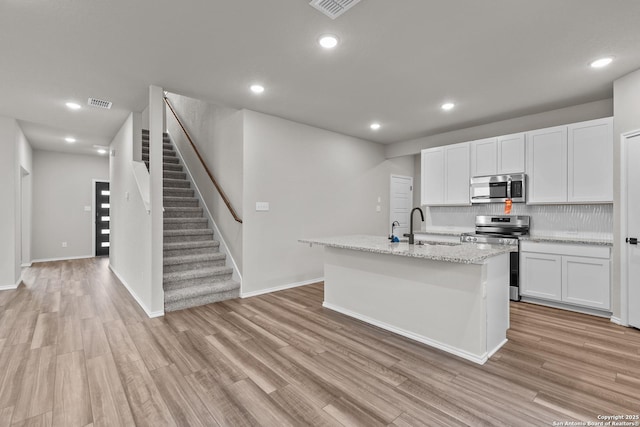 kitchen featuring sink, appliances with stainless steel finishes, a kitchen island with sink, white cabinets, and light wood-type flooring