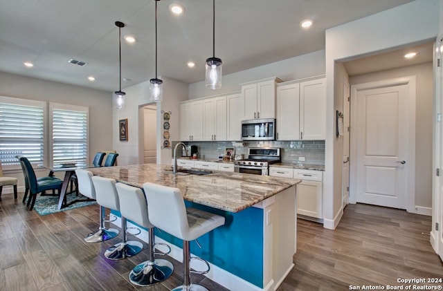 kitchen with appliances with stainless steel finishes, hardwood / wood-style floors, an island with sink, backsplash, and white cabinetry