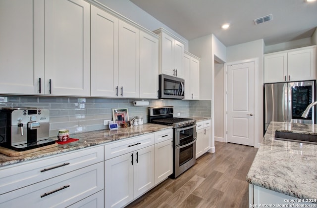 kitchen with white cabinetry, appliances with stainless steel finishes, light stone countertops, light hardwood / wood-style floors, and tasteful backsplash