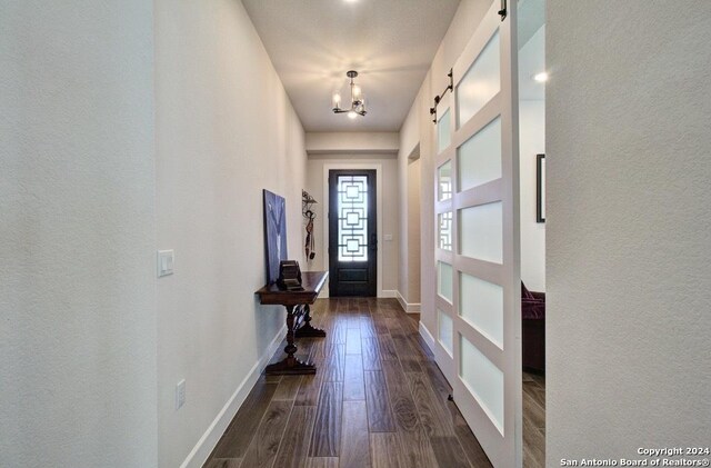 doorway with a notable chandelier, dark hardwood / wood-style floors, and a barn door