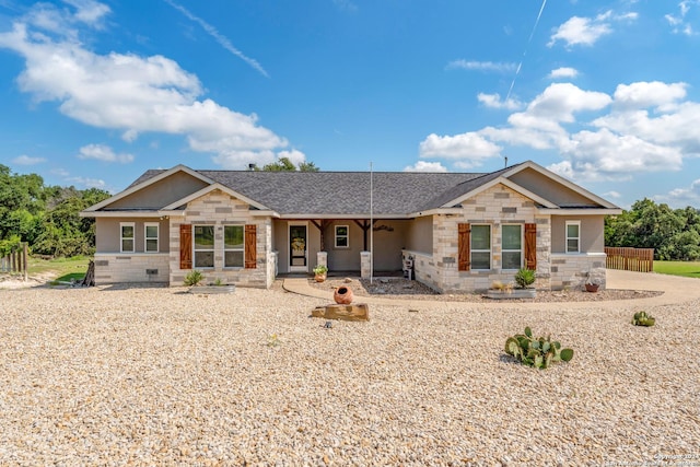 view of front of property with stone siding, roof with shingles, and fence